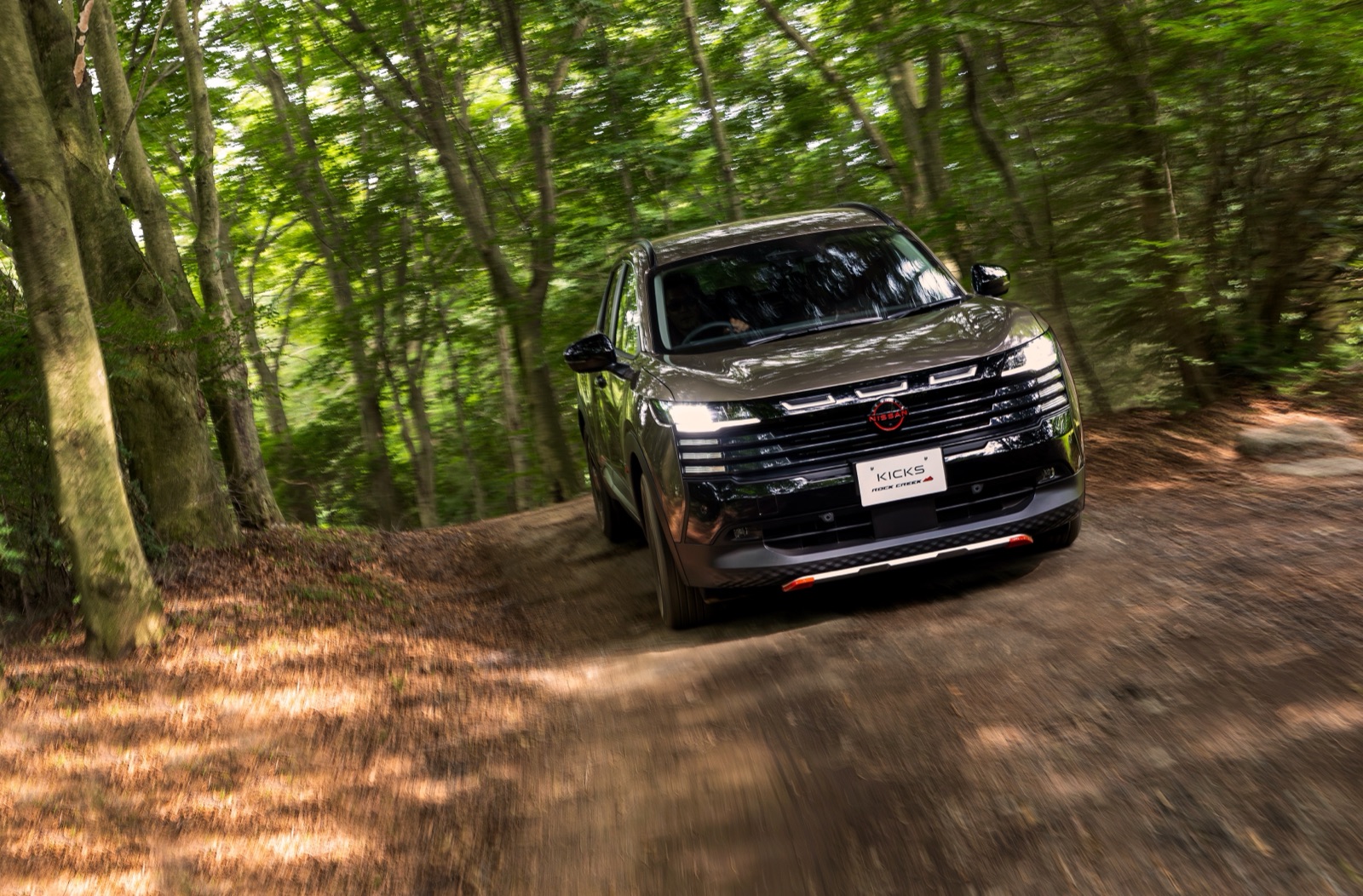 森の中の未舗装路を走る日産 キックス ROCK CREEK。アウトドア志向のカスタムカーとしての位置づけを示す
