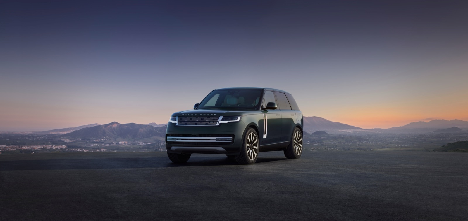 夕暮れの高台に佇むRANGE ROVER ELECTRIC。遠景に山並みを望むフロント斜め前方の全景